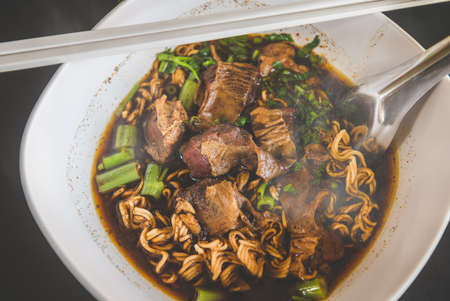 Braised pork noodles in Thai style with indoor low lighting.の写真素材