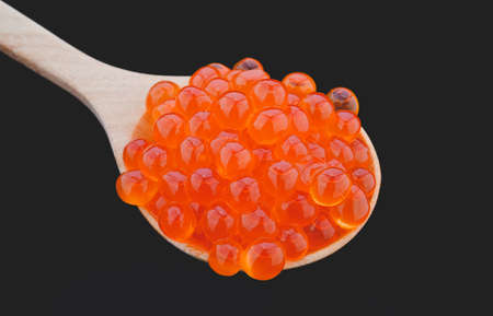 Salmon roe in wooden spoon with black background.