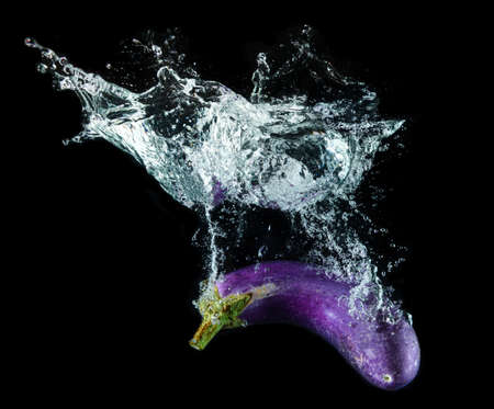 Water splashing and purple eggplant with black background.の写真素材