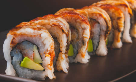 Unagi roll or Japanese grilled eel roll with rice and avocado cut and serve with dark background.の写真素材