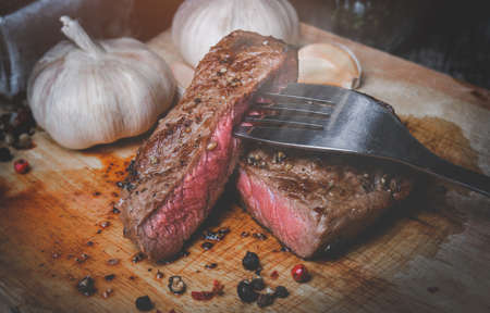 Medium rare beef steak cut slice on wooden plate with low lighting.の写真素材