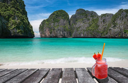 Maya bay island view with wooden board and cold drink glass in sun lighting.の写真素材