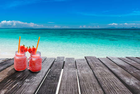 Blue clear sea view with wooden board and cold drink glass in sun lighting.の写真素材