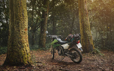 Adventure traveling enduro motocycle in mountain forest with low lighting and dark shadow.の写真素材