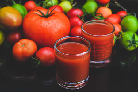 Mix tomatoes and juices in glass with black background lowlighting.の写真素材