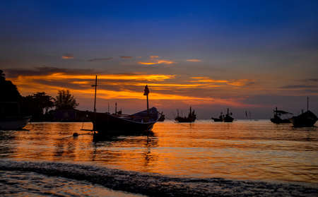 Silhouette fishery boats in the sea with sunset warm low lighting and dark shadow.の写真素材