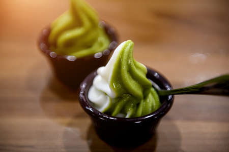 Matcha green tea ice cream in a cup on a wooden table with low lighting.の写真素材