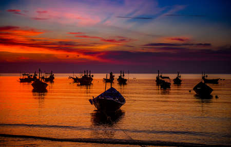 Silhouette fishery boats in the sea with sunset warm low lighting and dark shadow.の写真素材