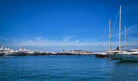 Boats and yachts anchored or moored in a marina and by its promenade on a bright summer day....