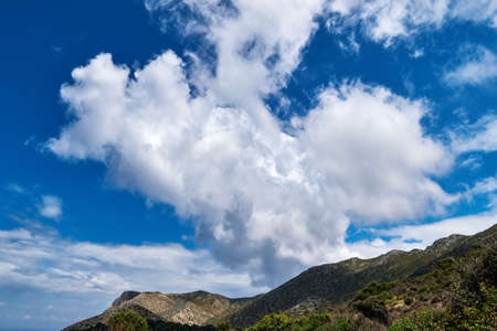 Great dynamic clouds in beautiful blue sky over hills and slope at daytime. Typical Greek landscape in spring.の写真素材