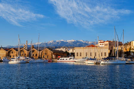 Old Venetian port, Chania, Crete, Greece. Sailboats, yachts, pier, shipyards or Arsenali Veneziani or Neoria. Bell tower and minaret, Cretan mountainsの写真素材