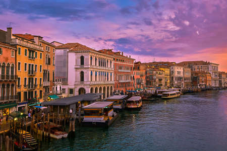 Sunset view of Grand Canal, Venice, Italy. Vaporetto or waterbus station, boats, gondolas moored by...