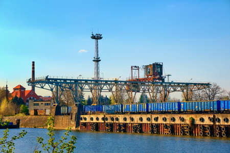 Old railway gantry crane used in river port for loading open-top gondola cars on sunny day....