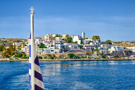 Greek flag and blurred typical Greek island landscape background. Bright summer day. Island hopping, adventures and exploring Mediterranean sea.の写真素材