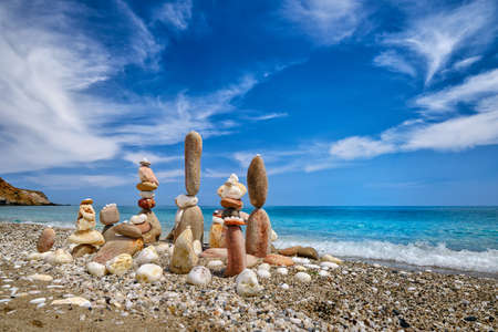 Group of balancing stones on beach. Bright sunny day, summer vibe, azure sea wave splash on pebble shore, blue sky and light cloudsの写真素材