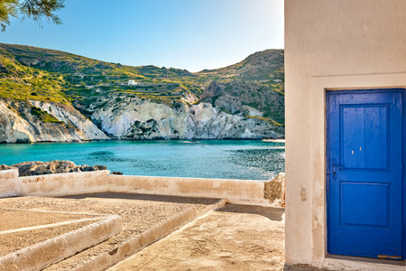 Sunny summer landscape, whitewashed terrace, blue door and green hills. Traditional Greek house by seafront. Milos island, Greeceの写真素材
