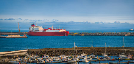 Panoramic shot of LNG or liquified natural gas carrier moored by industrial pier on hazy evening....