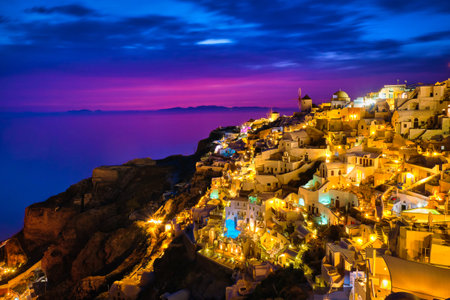 Beautiful view of Oia village with traditional whitewashed houses and windmills, Santorini island, at sunset, Greece. Scenic travel background, famous destination, colorful sky and clouds.の写真素材