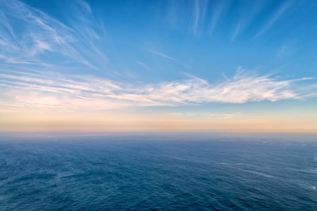 Beautiful seascape with calm sea or ocean waves. Atmospheric haze, colorful low clouds lit by sundown at horizon, high romantic clouds in clear blue sky. Beauty in nature, idyllic landscape, perfect background, natural backdrop.の写真素材