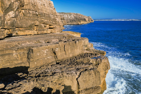 Beautiful cliffs and rock formations in Peniche, Portugal, on sunny day. Weathered rock formations, geological interest, cliffs, blue sea waves, tide, coastline, clear blue skyの写真素材