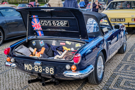 Lisbon, Portugal - Jan 20, 2024: Open trunk full of assorted items and stickers and rear side of classic Triumph Spitfire MK3 car parked on cobblestone path by another vintage vehicle showcasing the elegance and design of early automotive engineeringのeditorial素材