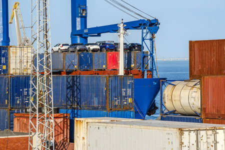 Cargo and tank containers stacked with cars on top on bulk carrier in sea port on sunny day....