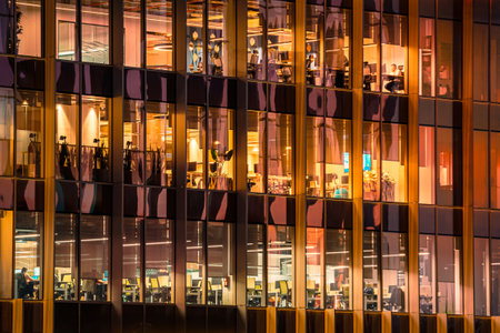 Contemporary office building at night with large glass windows revealing warmly lit workspaces....