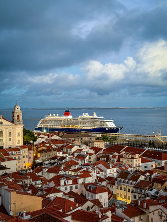 Large cruise ship moored in historic center of Lisbon, Portugal. Alfama area full of original buildings with red-tiled rooftops, high church bell tower, cloudy sky at afternoon. Travel destination, voyage, cruise liner, tourist attraction, landmarkの写真素材
