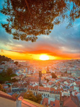Colorful sunset over Lisbon, Portugal, vibrant cloudy sky, bright sun setting behind April 25th or 25 de Abril bridge, over rooftops, Tagus or Tejo river, Sao Jorge castle hill. Travel destination, tourist attraction, sundown landscape, cityscapeの写真素材