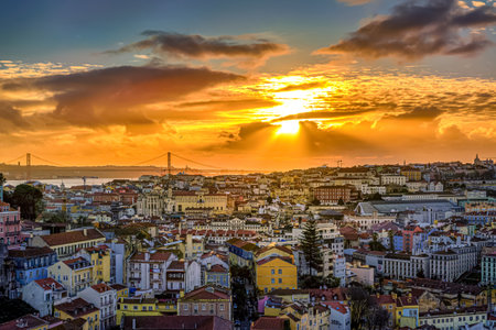 Beautiful sunset over cityscape of Lisbon, Portugal, historic center, Tagus river with dramatic clouds, famous Ponte 25 de Abril or April 25th bridge silhouette, sunlight, colorful tiled rooftops. Glowing sky, popular travel destination, iconic viewの写真素材