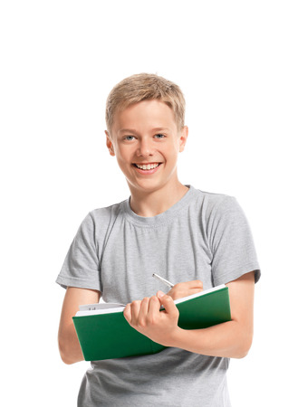 Happy teenage boy writes something in a notebook. Isolated on white background の写真素材