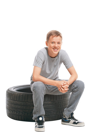 Smiling teenager sitting on a car tire. Isolated on white backgroundの写真素材