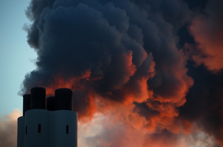 Pollution concept of smoking chimney  The setting sun illuminates the vapor from below, giving it an ominous impression, like that of volcano smoke の写真素材