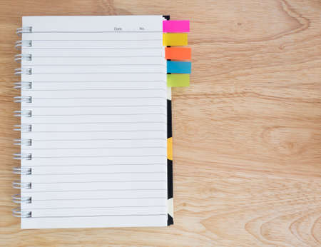 Blank notebook and colorful sticky note on wood background