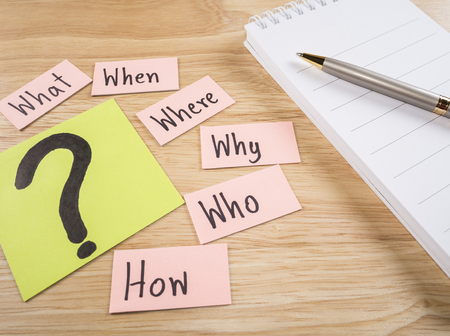 Questions what, when, where, why, who, how and white notebook with pen on wood backgroundの写真素材