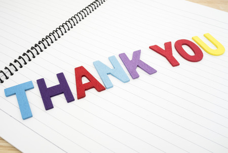 Word spelling "Thank you" on white notebook with wood backgroundの写真素材