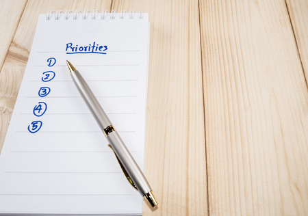 Priorities on blank notebook with a pen on wooden background (Business concept)
