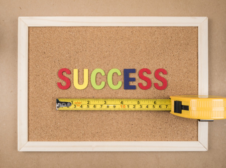 Word spell success by wooden font and measuring tape on cork board (Business concept)