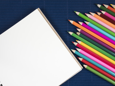 Stack of color pencil and blank notebook on blue corrugate paper background (Business object)の写真素材