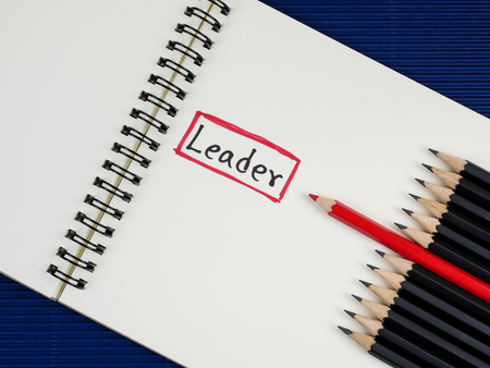 Red pencil standout from black pencil and handwriting word Leader on blank notebook with blue corrugate paper background, leadership business conceptの写真素材