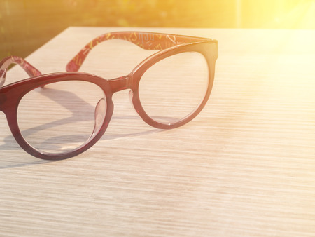 Eye glasses on wood table in the coffee shop under sunlight in the morning with warm / soft color...