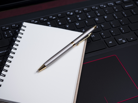 White blank notebook and pen on laptop keyboard (Selective Focus)