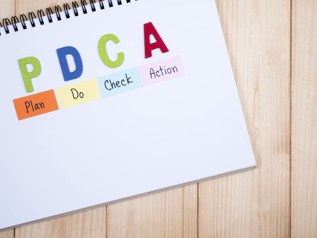 Wooden word PDCA and handwriting Plan, Do, Check, Action) on notebook in wood background (Business Concept)の写真素材