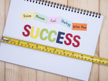 Wooden word Success and handwriting Vision, Mission, Goal, Strategy, Action Plan on notebook with wood background (top view)の写真素材