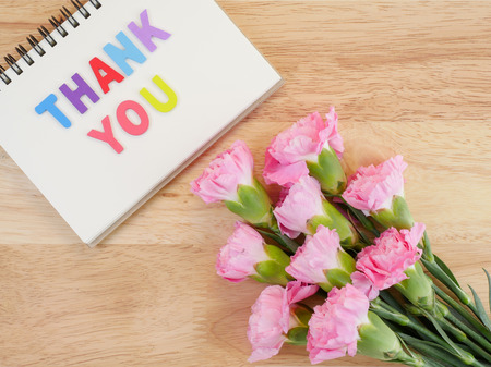 Word spell Thank you on notebook and bouquet of sweet pink Carnation flower on wood background with top viewの写真素材