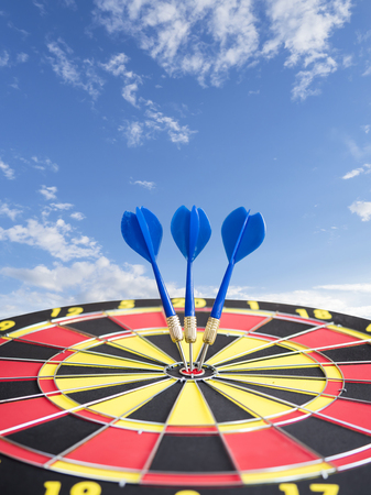 Dart arrows pin in the center of dart board with blue sky background (Business Concept)の写真素材