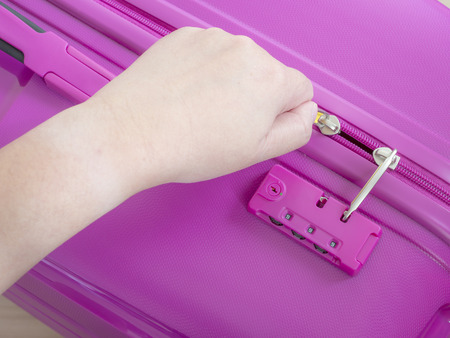 Woman use left hand to close zipper on pink suitcaseの写真素材