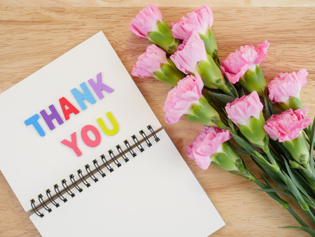 Font Thank you on blank notebook and bouquet of Carnation flower with wood background on top viewの写真素材