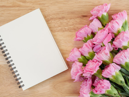 Blank notebook and bouquet of sweet pink Carnation flower on dark wood background with top viewの写真素材