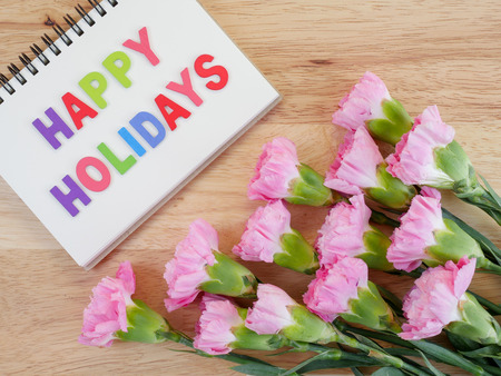 Wooden word spell Happy Holidays and sweet pink carnation flower on wood background with top viewの写真素材